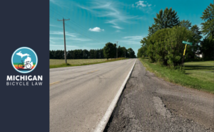 Deteriorating road shoulder alongside a rural Michigan roadway, illustrating maintenance issues that cyclists may encounter when riding in bike lanes and shoulder areas.