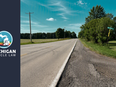 Deteriorating road shoulder alongside a rural Michigan roadway, illustrating maintenance issues that cyclists may encounter when riding in bike lanes and shoulder areas.